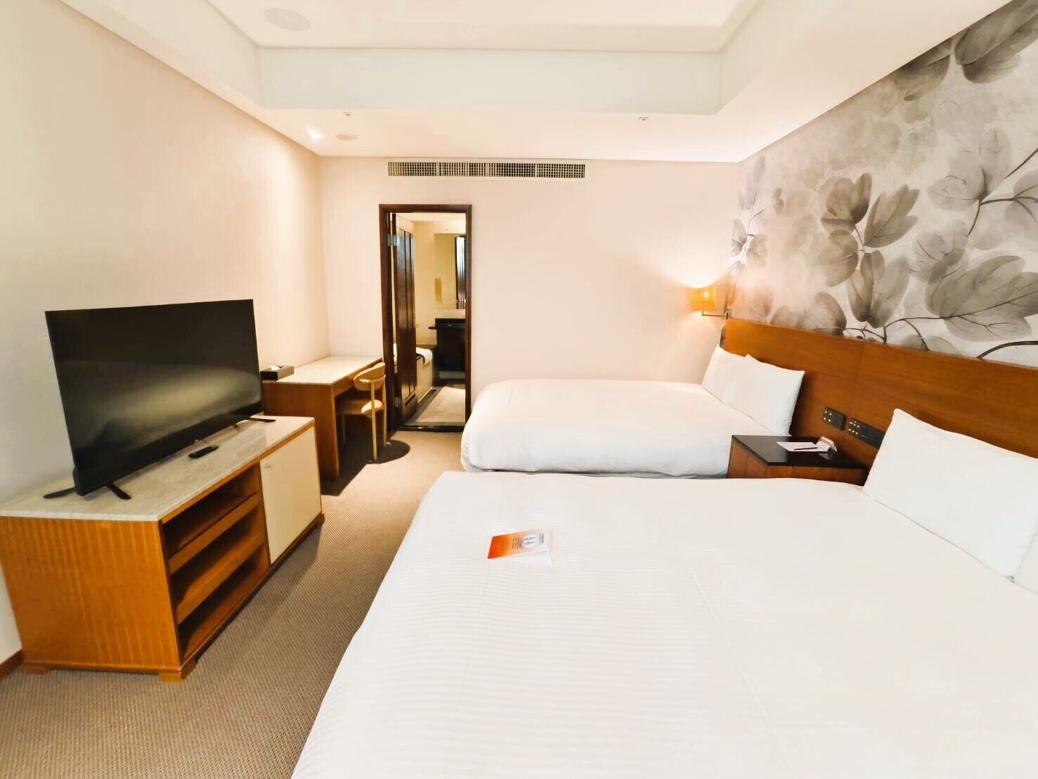 A hotel room with a bed, a TV, a desk, and a bathroom visible through an open door.