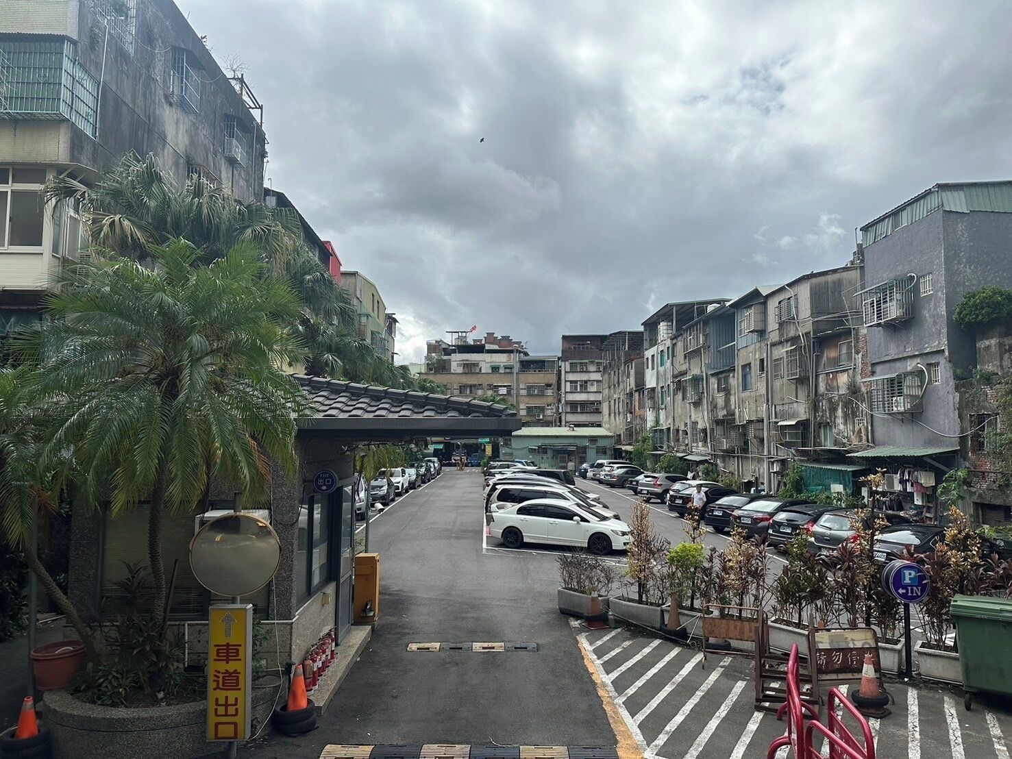 A street view with parked cars, a pedestrian crossing, and buildings with balconies.