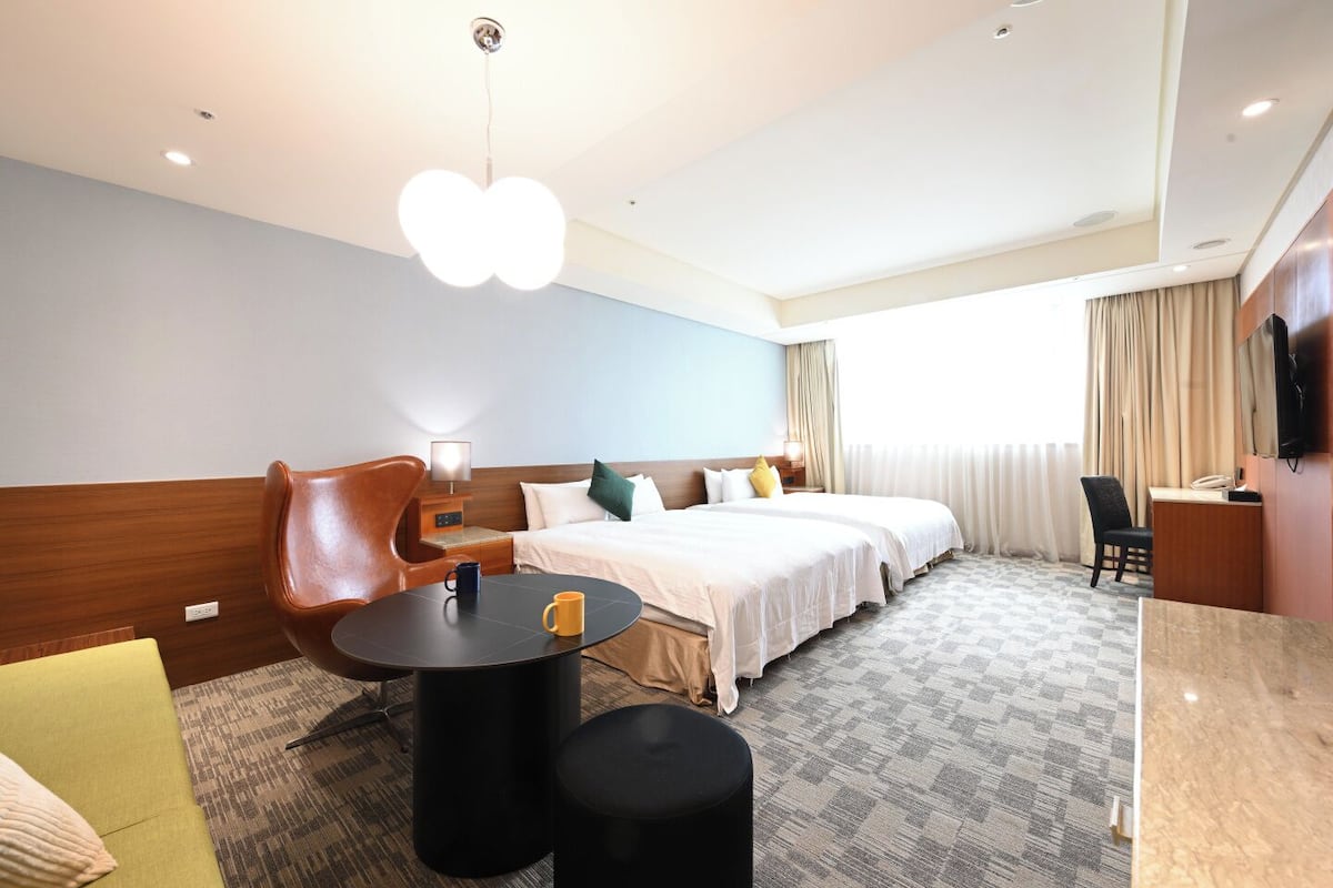 A hotel room with a bed, a desk, a chair, a coffee table, and a unique ceiling light fixture.