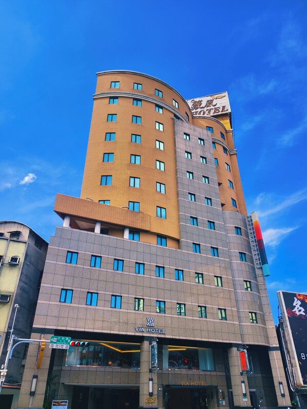 A multi-story hotel with a prominent Via Hotel sign, featuring a modern design with a mix of brick and glass facades, and a curved corner structure. - Via Hotel Breeze (New Taipei City)