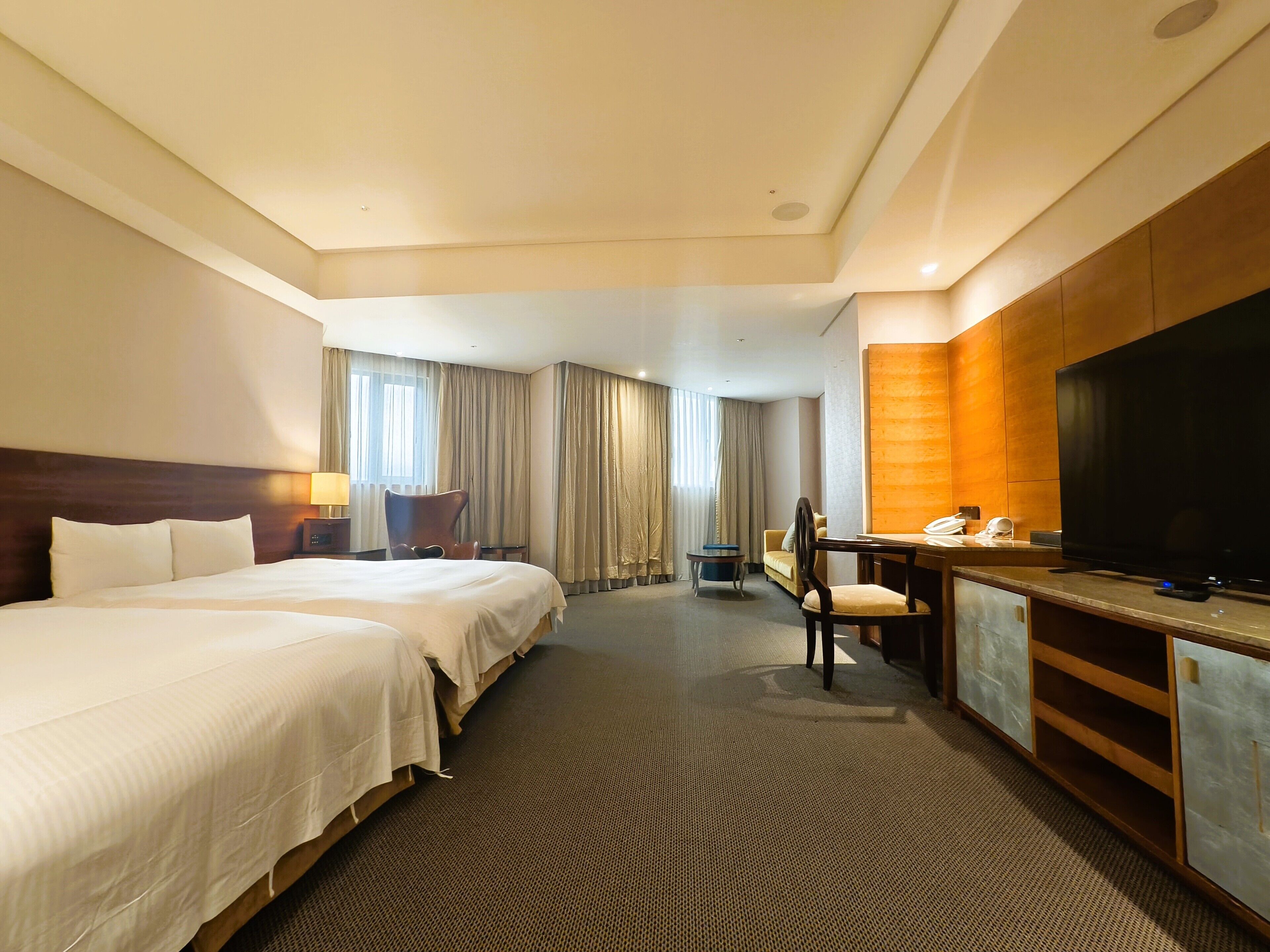 A hotel room with a large bed, a desk with a flat-screen TV, a chair, and a small table.