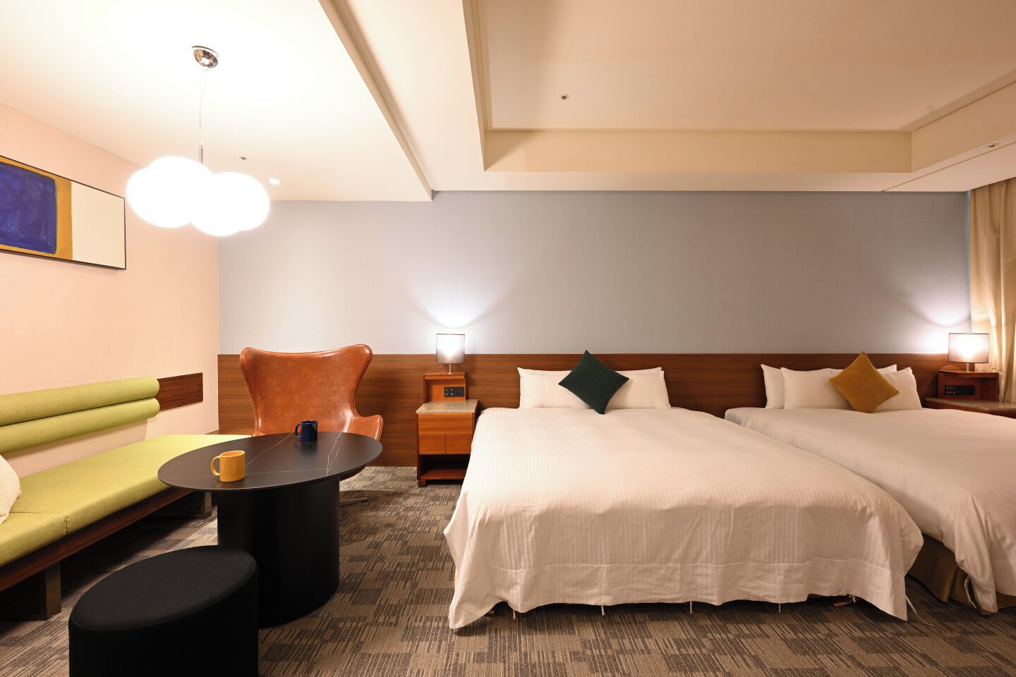 A hotel room with two beds, a sofa, a small table, and a lamp.