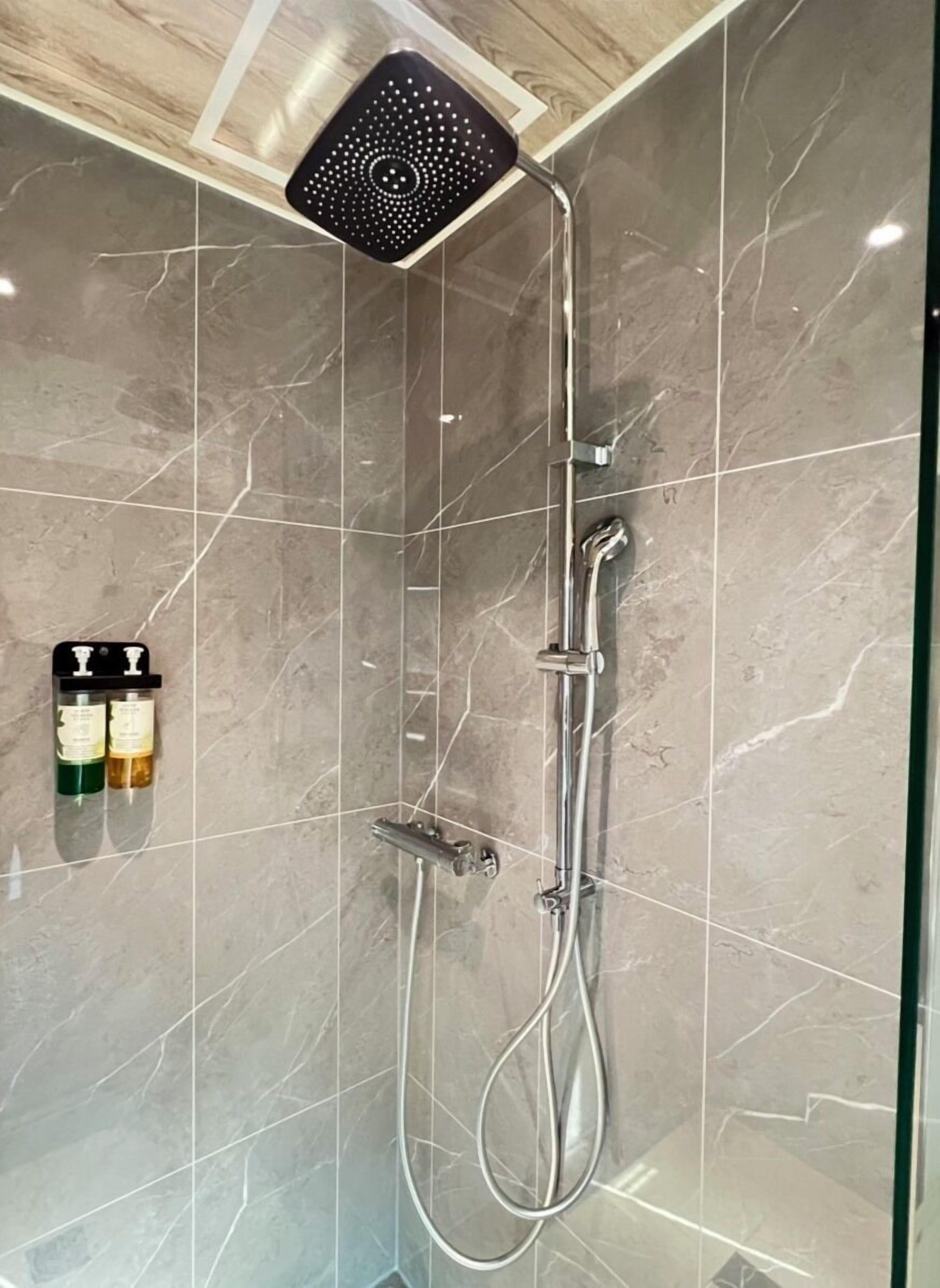 A shower with a handheld showerhead, a wall-mounted control, and a handheld showerhead.