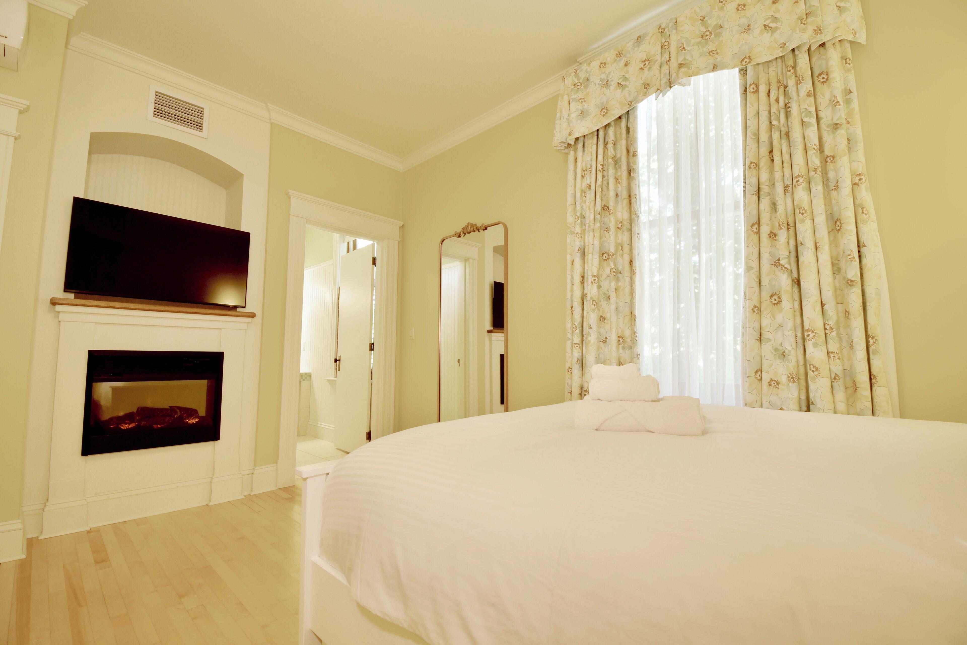 Un dormitorio con una cama grande, chimenea, televisión y espejo.