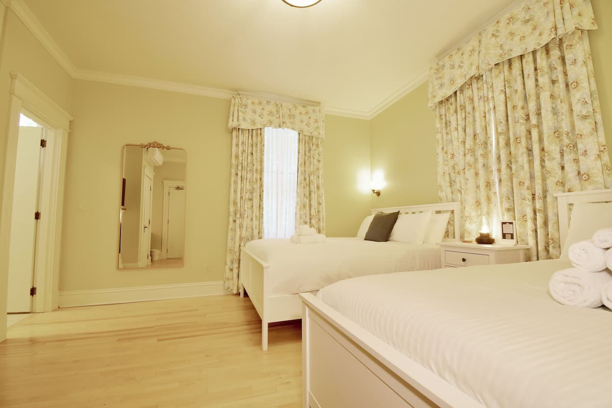 A hotel room with two single beds, a large mirror, a bedside table with a lamp, and a window with floral curtains.