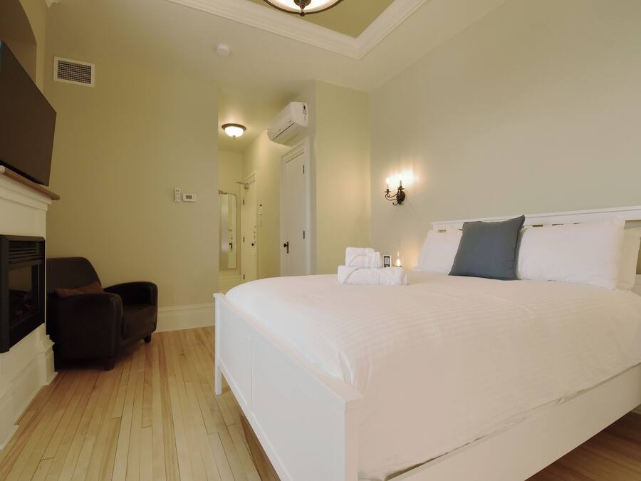 A bedroom with a large bed, a chair, a TV, and a fireplace.