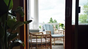 Una terraza de madera con sillas de mimbre y una mesa, baranda blanca y una planta en maceta.