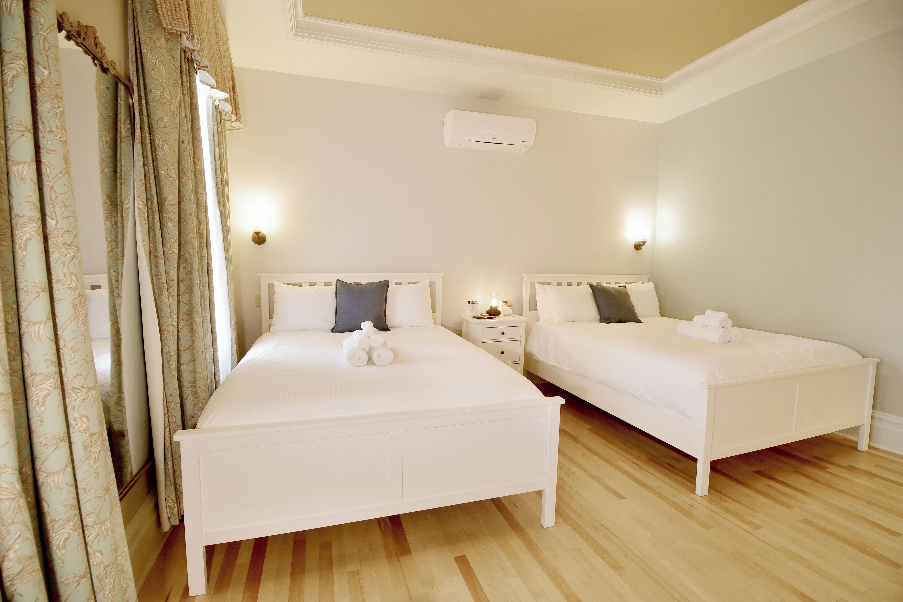 A double room with two beds, a bedside table with a lamp, and a ceiling-mounted air conditioner.