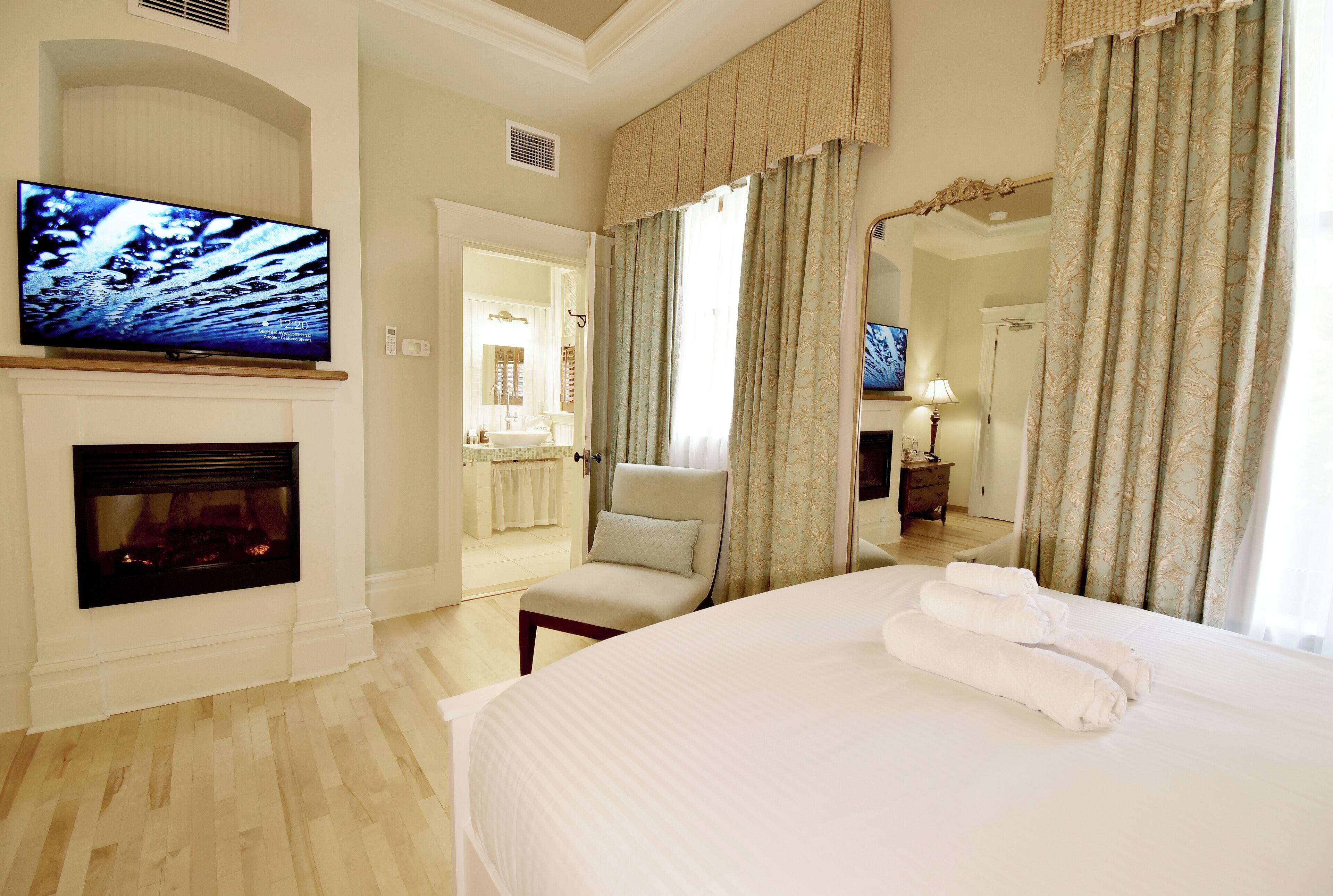 A hotel room with a fireplace, a television, a bed with towels, a chair, and a mirror.