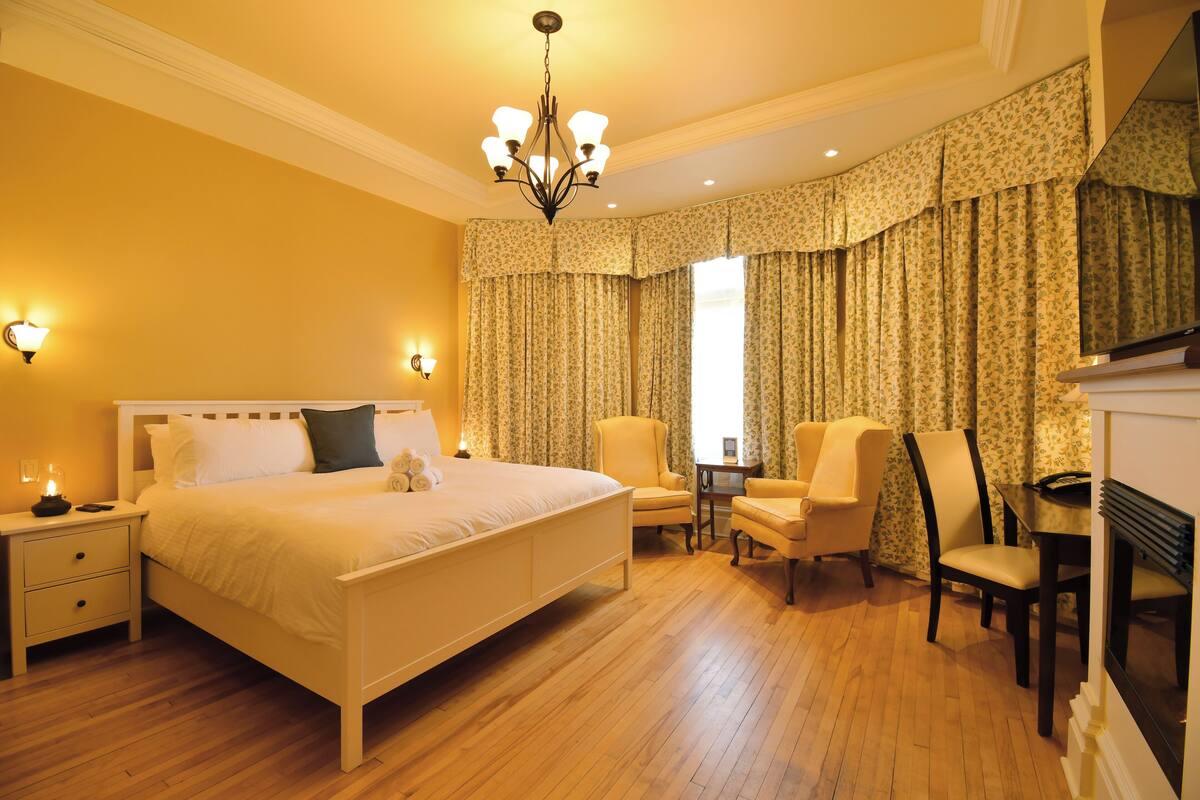 A bedroom with a large bed, two chairs, a small table, and a fireplace.