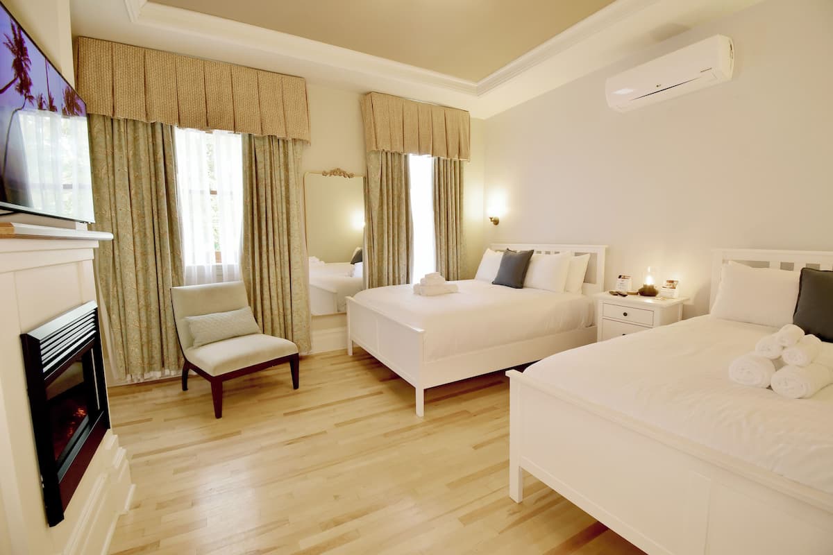 A hotel room with a large bed, a smaller bed, a chair, a nightstand, an air conditioning unit, and a fireplace.