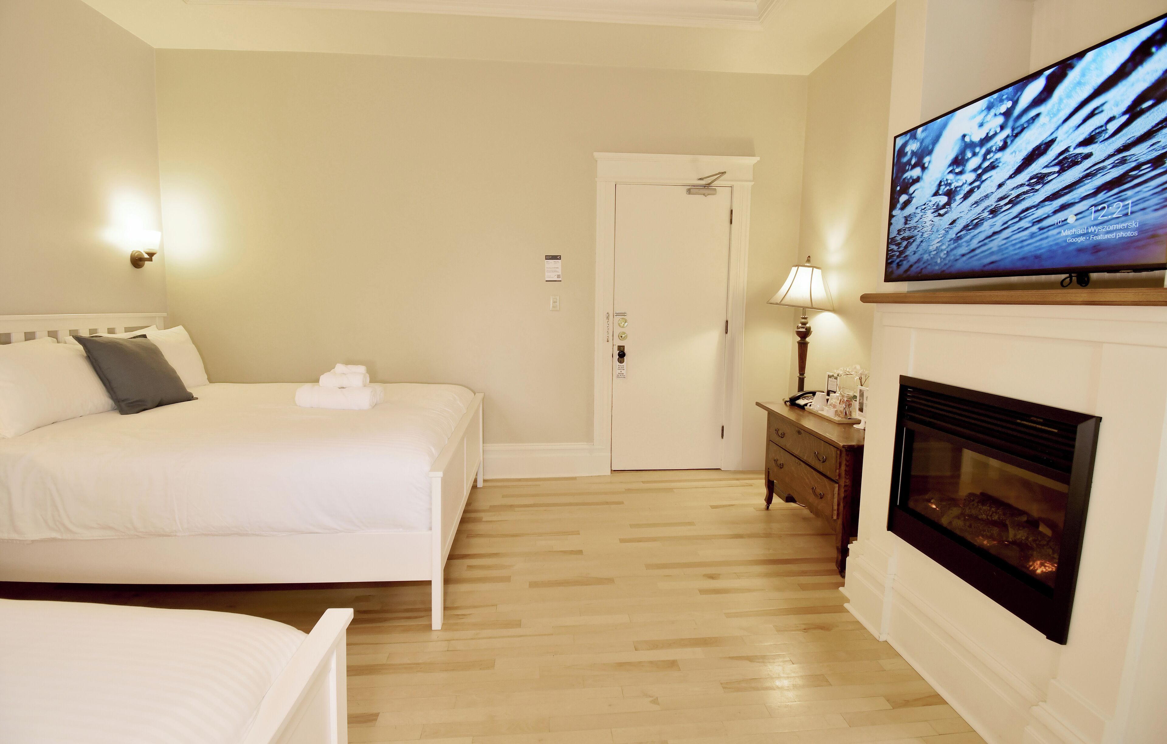 A hotel room with a bed, a TV, a fireplace, and a door.