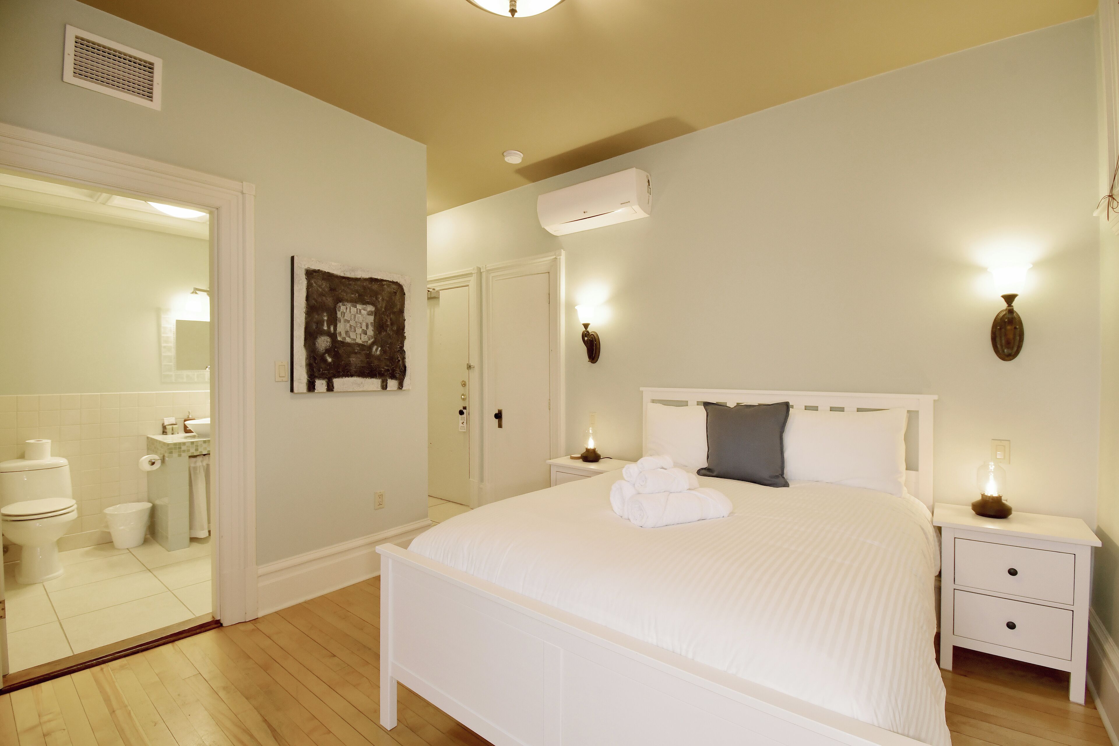 A bedroom with a large bed, a bedside table, a nightstand, a wall-mounted lamp, and a mirror.