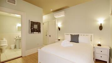 A bedroom with a large bed, a bedside table, a nightstand, a wall-mounted lamp, and a mirror.