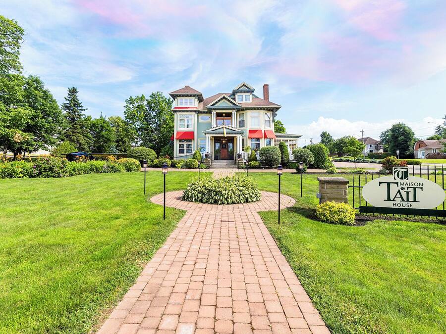 A large, two-story house with a brick pathway leading to the entrance, surrounded by well-maintained lawns and trees.