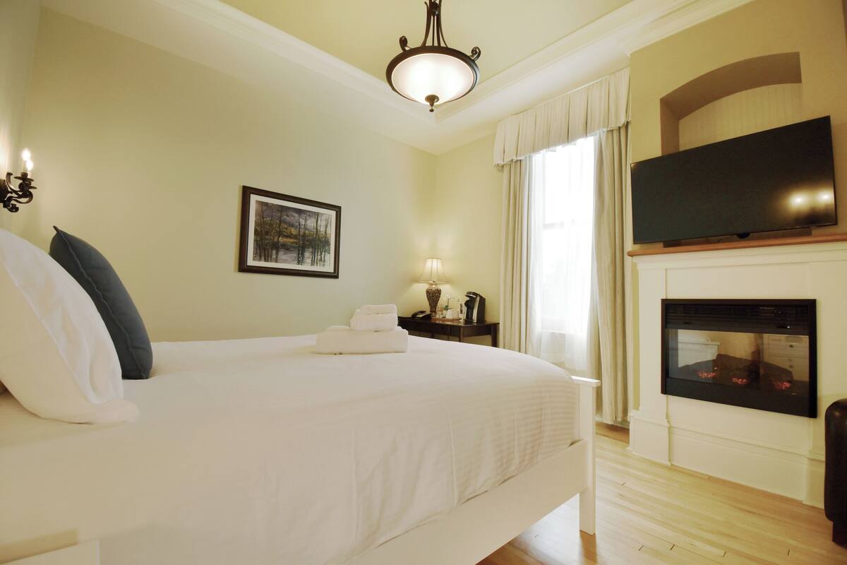 A hotel room with a large bed, a flat-screen TV mounted above a fireplace, and a framed picture on the wall.