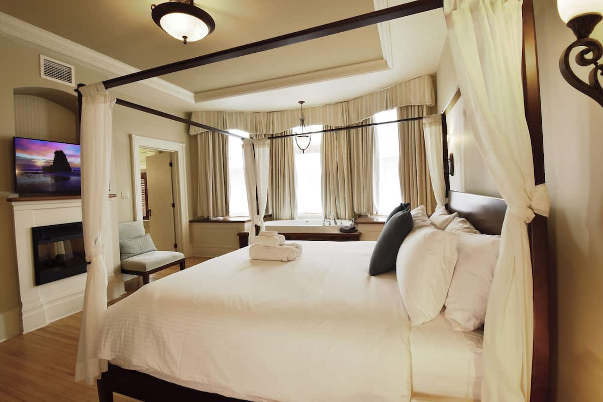 A four-poster bed with white linens, a flat-screen TV on the wall, and a fireplace.