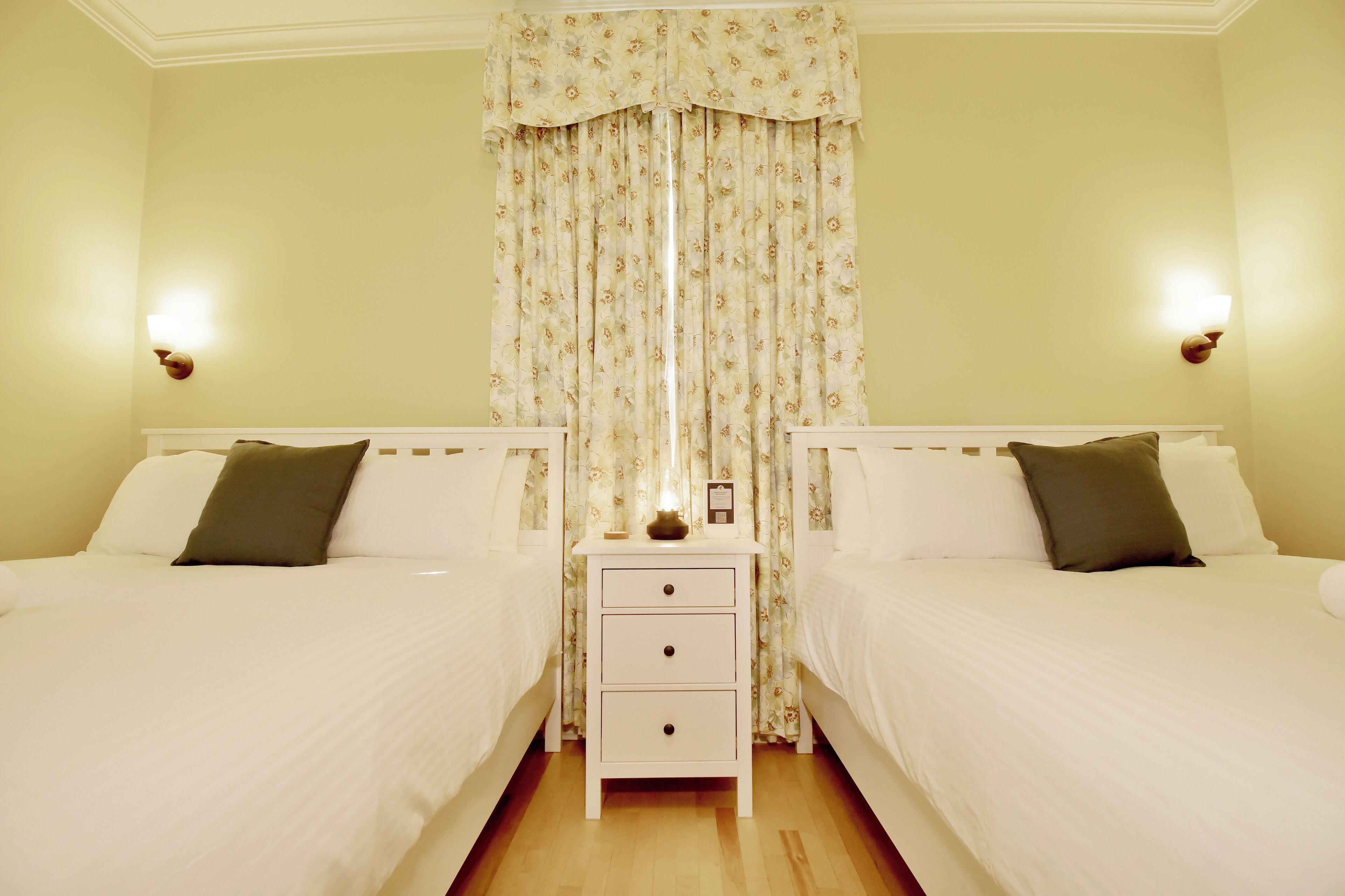 A double room with two beds, a nightstand with a lamp, and floral curtains.