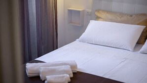 A neatly made bed with white linens and pillows, a small bedside table with a lamp, and a curtain partially drawn to the side. - Housestation  (Palermo)