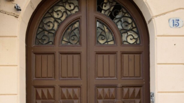 A double wooden door with decorative panels and a metal grille, set within an arched doorway. - Housestation  (Palermo)