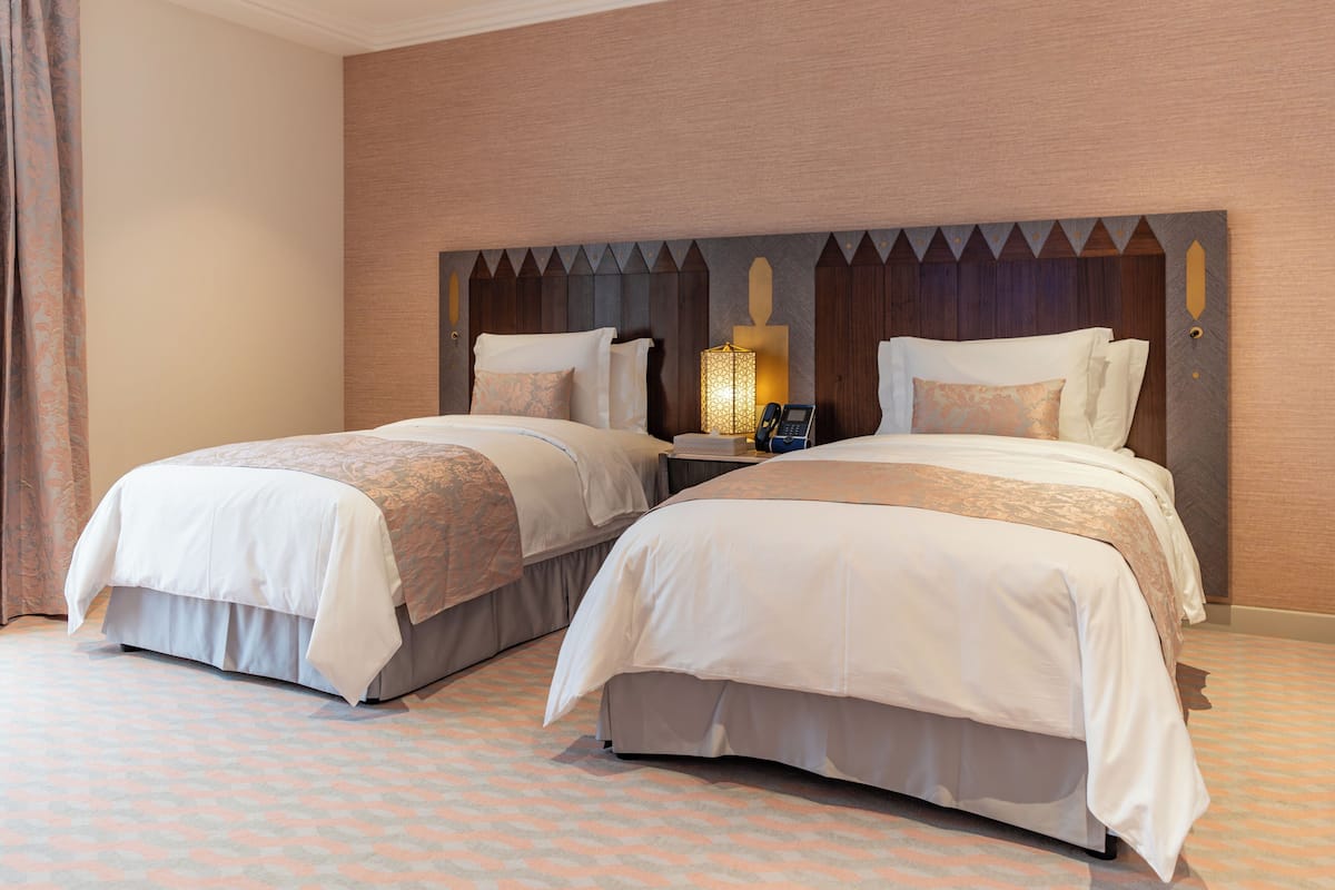 A hotel room with two beds, a nightstand with a lamp, and a patterned carpet.