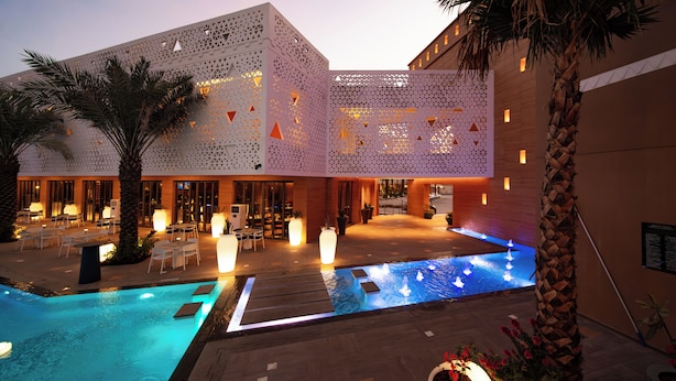 Un hotel moderno con zona de piscina, mobiliario exterior y una fuente decorativa.
