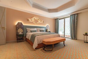 A bedroom with a large bed, a bench, a nightstand, and a wall-mounted light fixture. - Vivienda Hotel Villas Diplomatic Quarter (Riyadh)