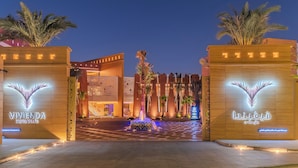 La entrada al Vivenda Hotel Villas, con una fuente central, palmeras y señalización iluminada.