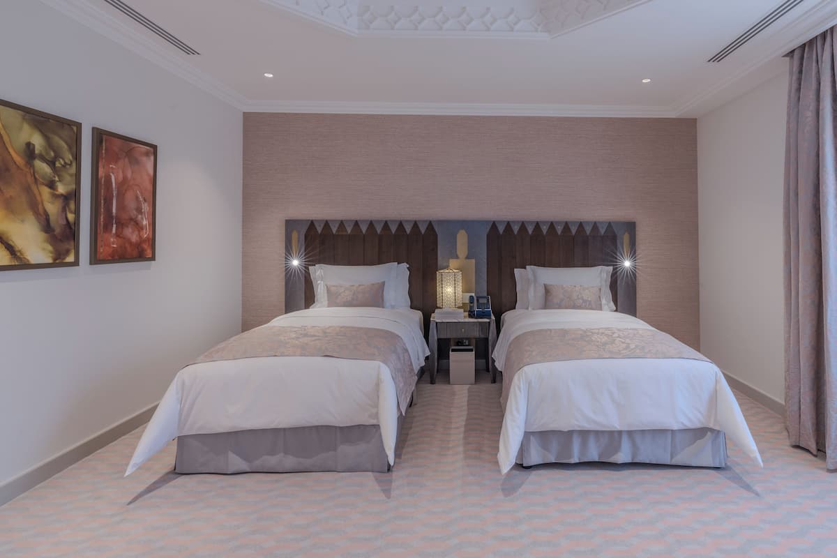 A hotel room with two beds, a nightstand, and a wall-mounted lamp.