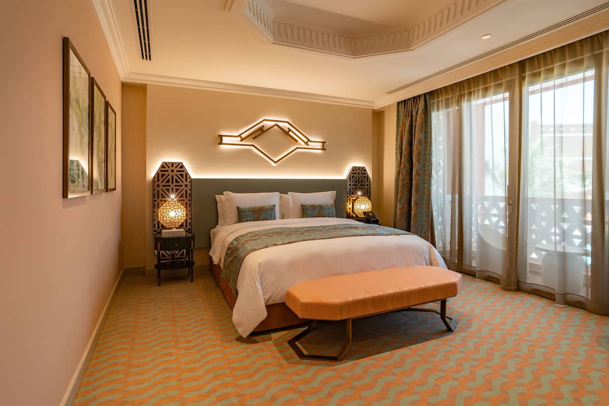A hotel room with a large bed, a bench, and a decorative wall piece.