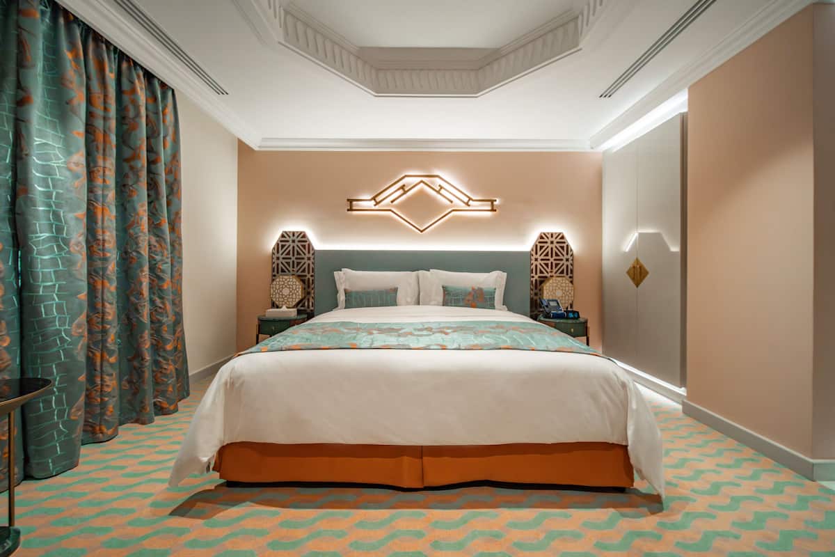 A hotel room with a large bed, a nightstand, a wall-mounted light fixture, and patterned curtains.