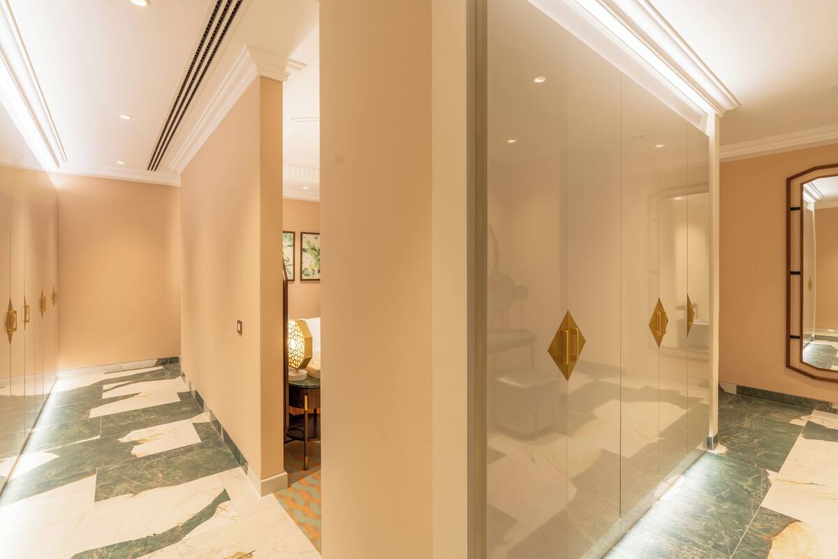 A hallway with a marble floor, glass doors, and a mirror on the right wall.