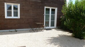 Ein Holzbau mit Fenster und TĂŒr, ein kleiner Tisch, zwei StĂŒhle und Kiesboden.
