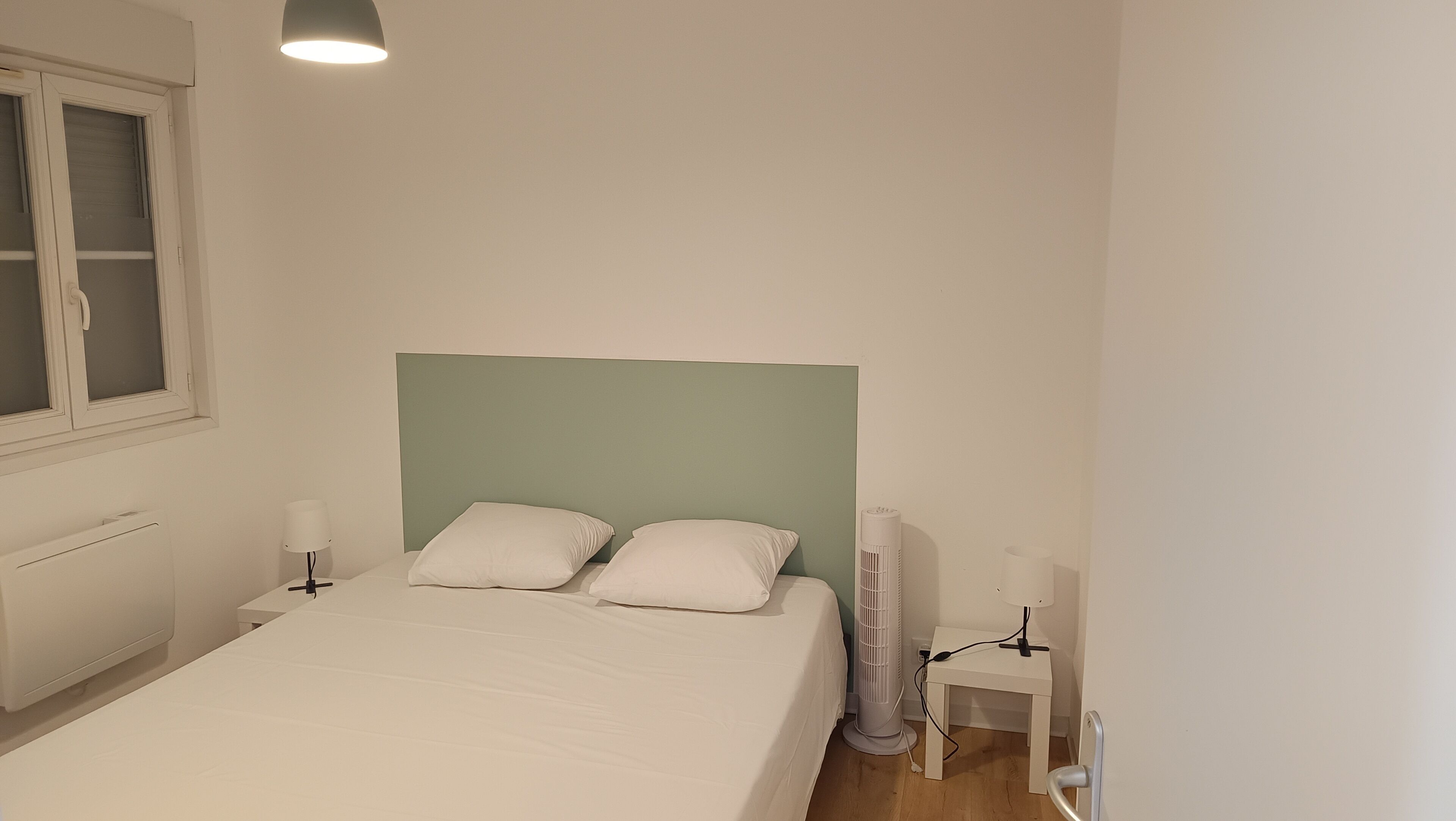 Una camera da letto con un letto, due lampade da comodino, un comodino, un termosifone e una finestra con persiane.
