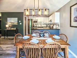 A dining area with a wooden table set for six, surrounded by wooden chairs. A chandelier hangs above the table. - Tranquil Toby / Hot tub / Ski out (Panorama)