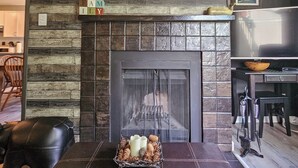 Ein Wohnzimmer mit Kamin, einer Bären-Dekoration, einem gerahmten Bild einer Berglandschaft und einer Sitzecke mit braunem Hocker.