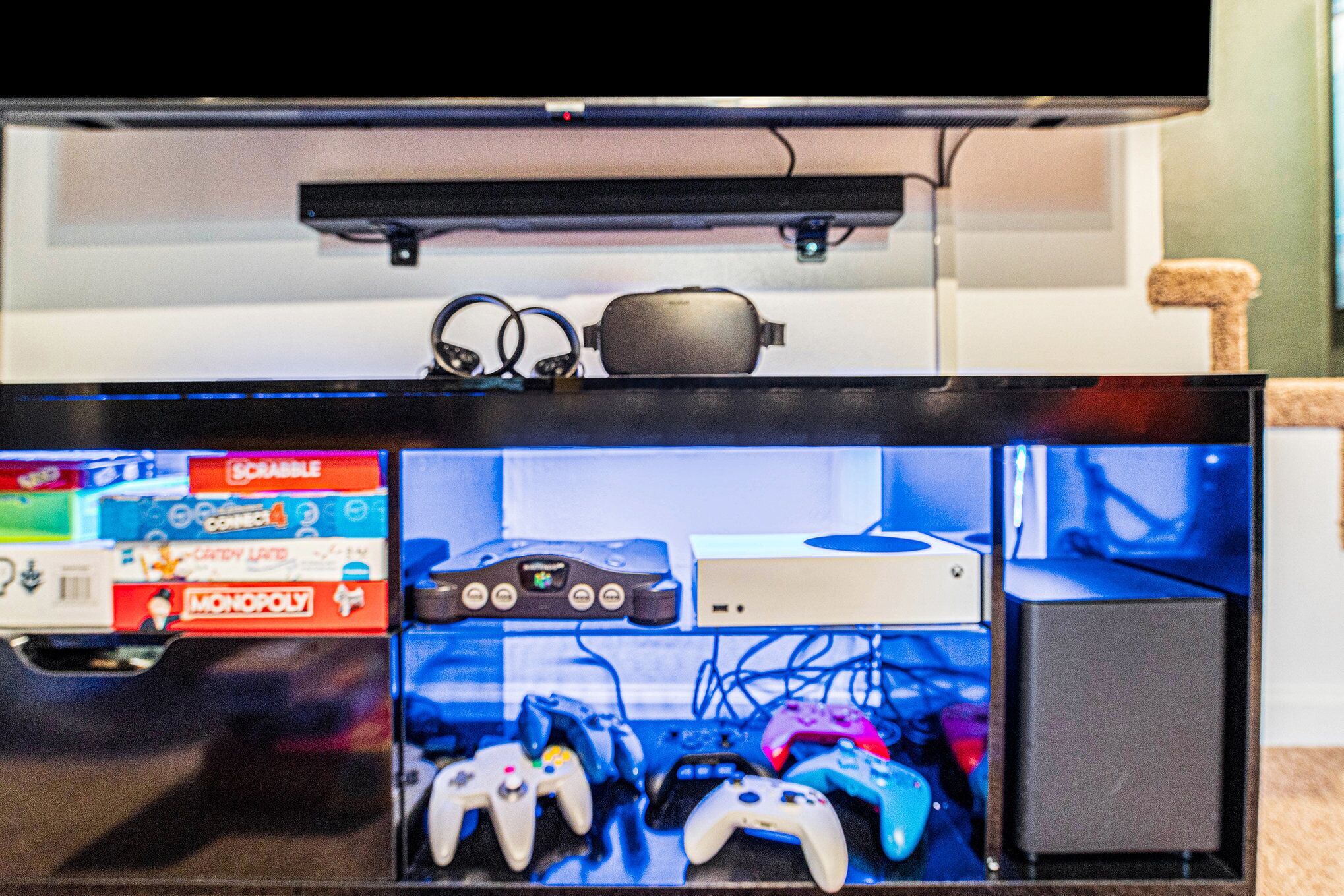 A television mounted on a wall with a gaming console and controllers below.