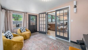 Una habitación con dos sillones amarillos, un tapete estampado y un gran ventanal corredero que da a un área exterior con terraza de madera.