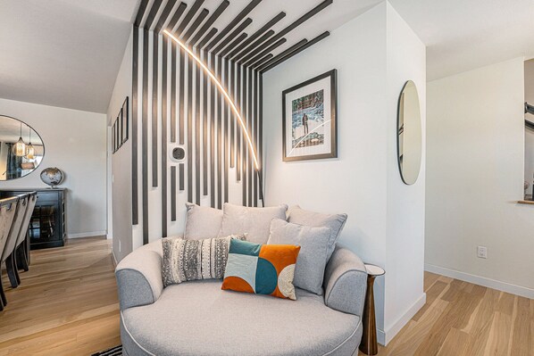 A modern living room with a round grey sofa, a wooden coffee table, and a striped wall design.