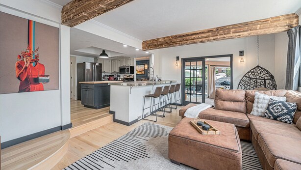 Una sala moderna con un amplio sofá modular marrón, una cocina con armarios blancos y un techo de madera.