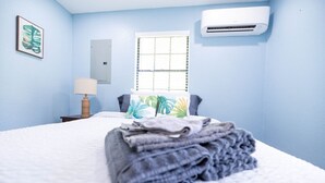 A bedroom with a bed, a window with blinds, an air conditioner, a nightstand with a lamp, and a framed picture on the wall. - Historic Oviedo Charmer - Close to everything (Oviedo)