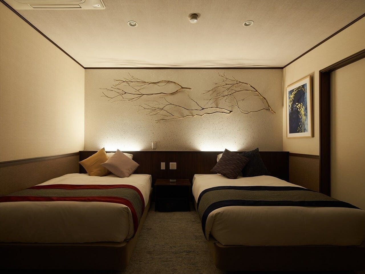 Habitación de hotel con dos camas, una obra de arte colgada en la pared, un cuadro enmarcado y una mesita de noche.
