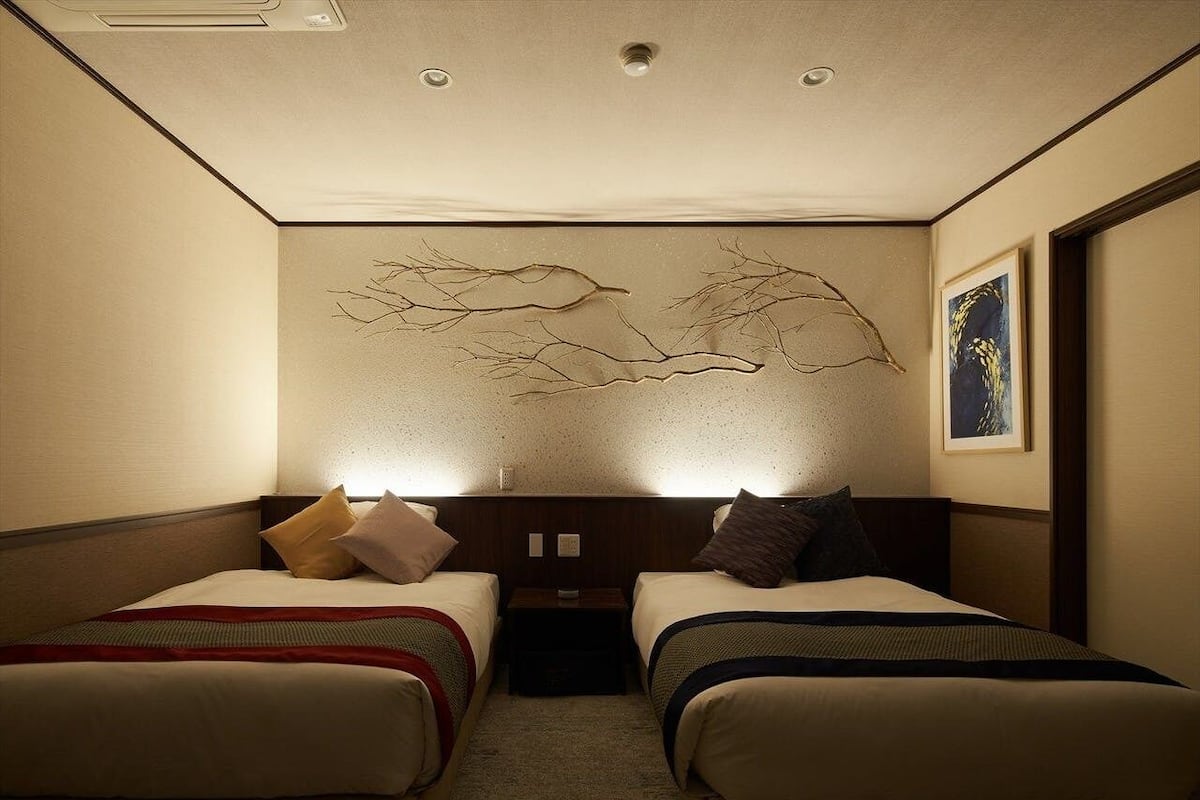 A hotel room with two beds, a wall-mounted artwork, a framed picture, and a nightstand.