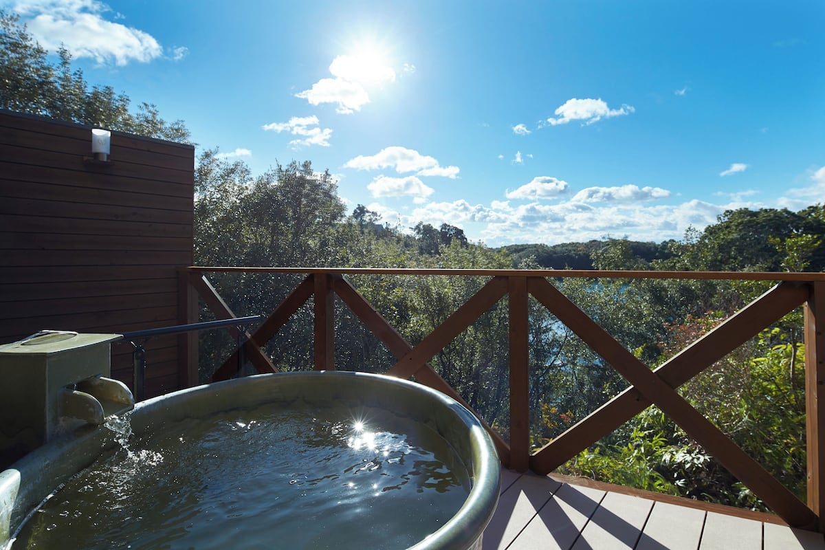 A hot tub on a wooden deck with a view of a forested area.