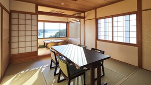 A traditional Japanese room with tatami flooring, a low table with chairs, and large windows offering a view of the outdoors. - Villa Ryusei (Shima)