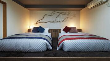 A double room with two beds, each with a checkered duvet, pillows in various colors, a wall-mounted artwork, and a ceiling-mounted air conditioning unit.