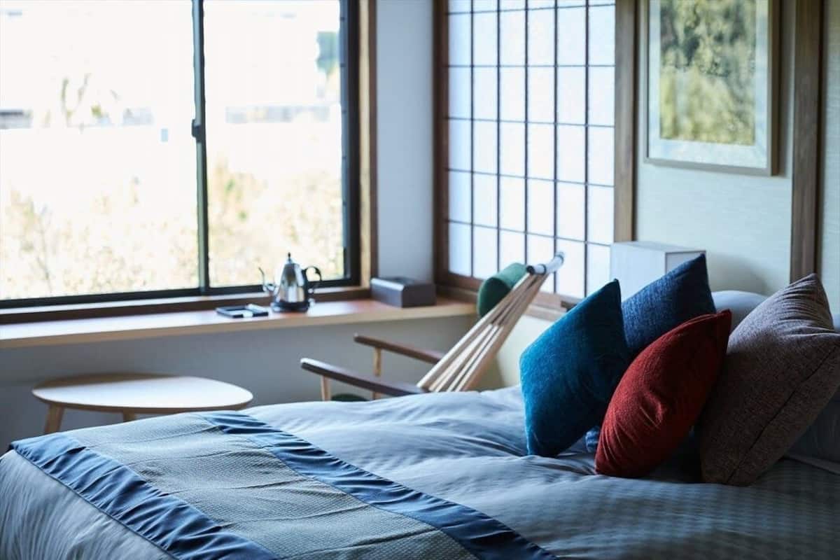 A bedroom with a bed, pillows, a window, and a small table.
