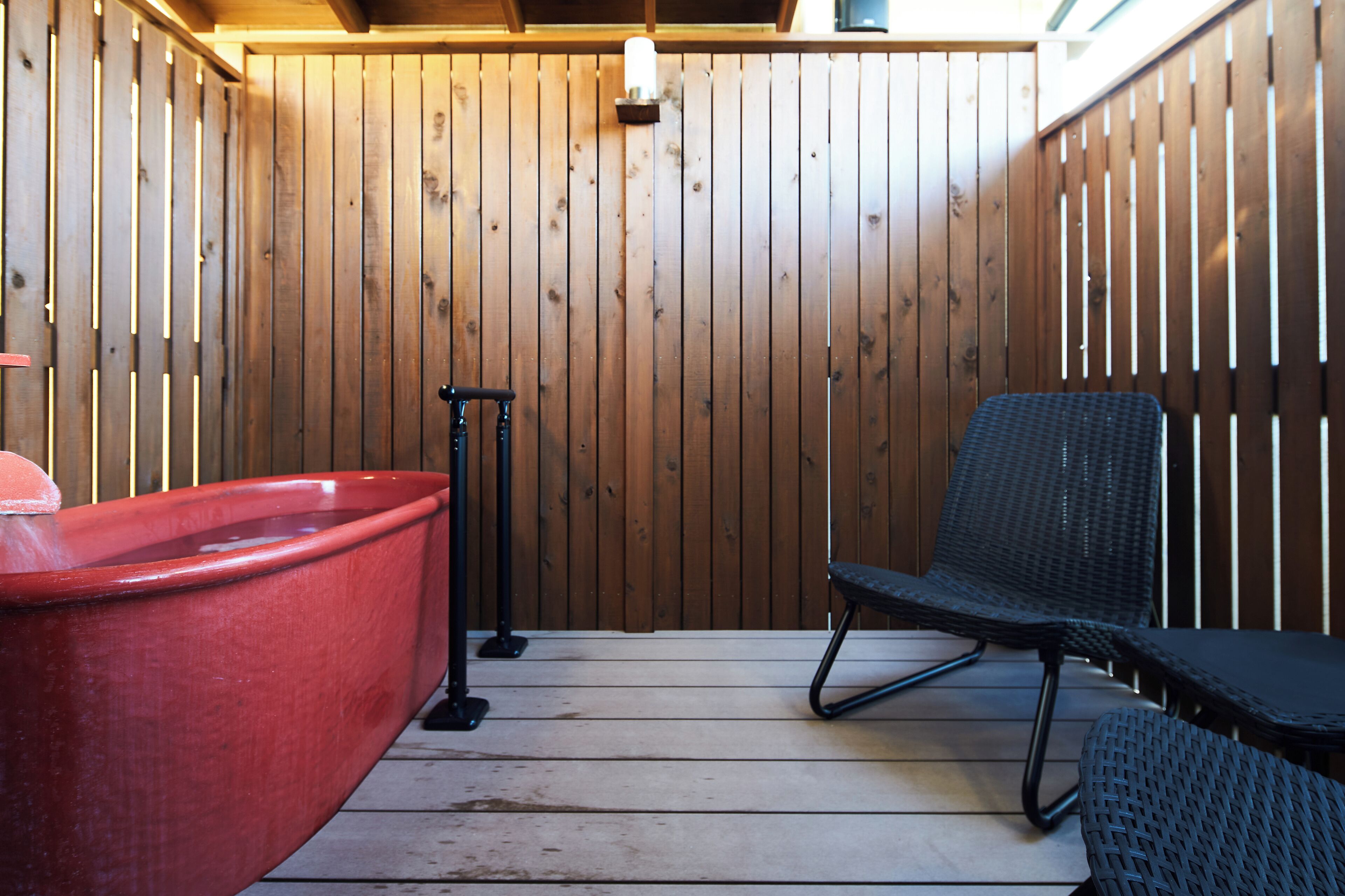 A wooden spa area with a red hot tub, a black chair, and a massage table.