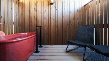 A wooden spa area with a red hot tub, a black chair, and a massage table.