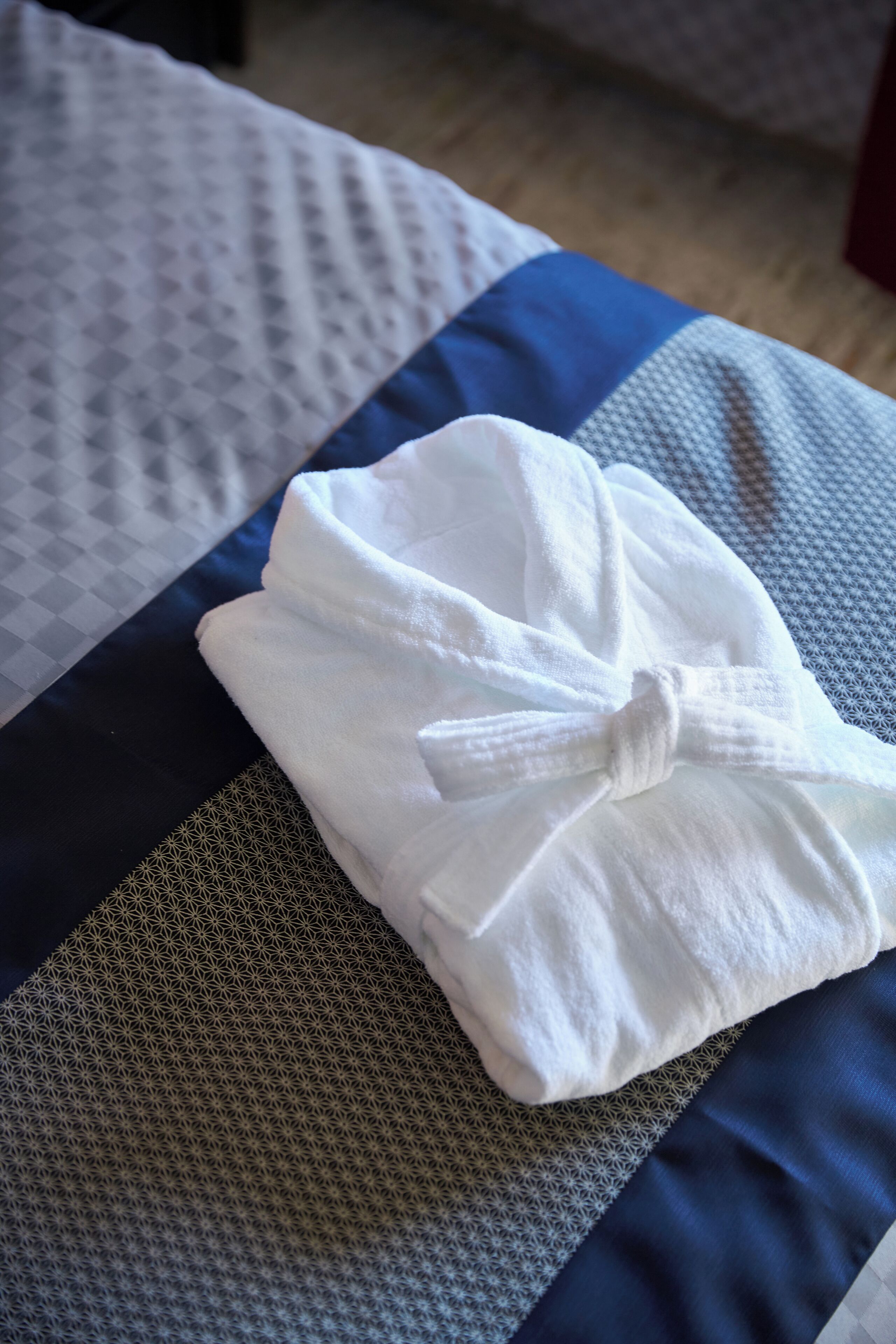 A neatly folded white towel on a bed with patterned bedding.